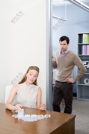 在办公室玩扑克牌的女人和倚在门边的男人图片