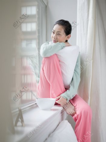 抱着枕头坐着窗台边的女人图片